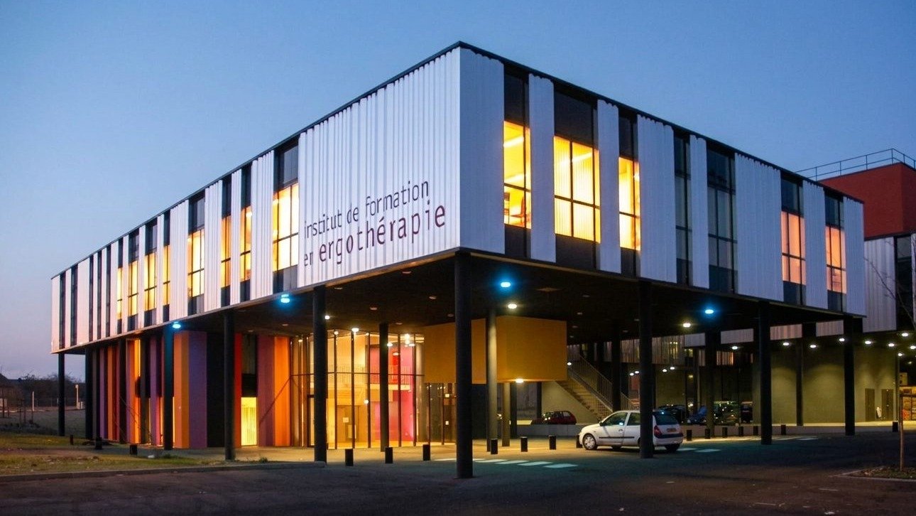 Façade éclairée de l'institut de formation en ergothérapie de Nancy, à la tombée de la nuit.